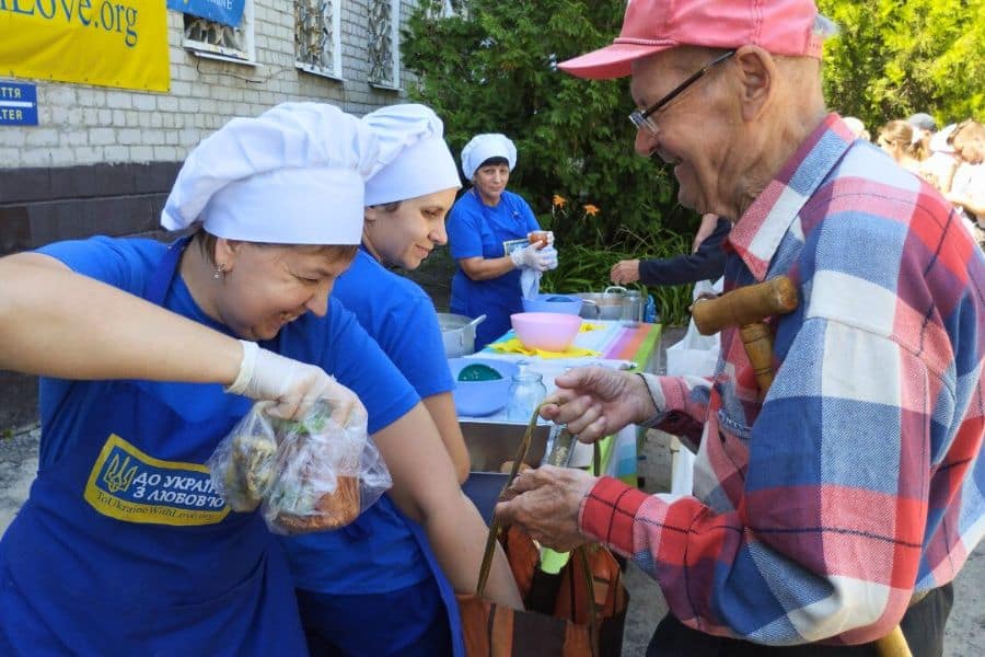 Volunteers of To Ukraine With Love serving hot meals to an elderly man